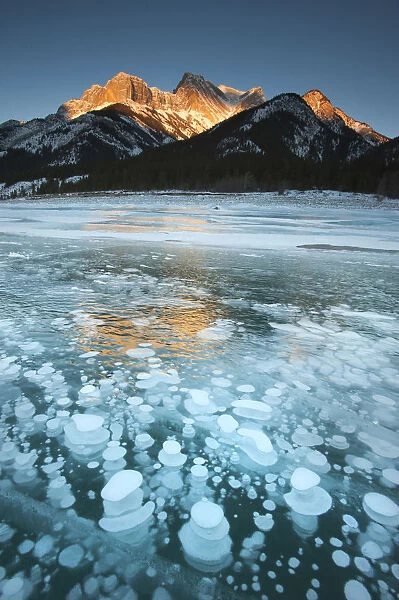 Mountains and frozen gas bubbles beneath surface of frozen lake, Abraham Lake, Canadian Rockies