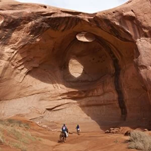 Horse riding trip, tourist with Navajo guide pass under rock arch, Monument Valley Navajo Tribal Park, Utah Arizona, United States of America, North America
