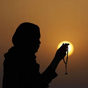 Silhouette of a Muslim woman holding prayer beads in her hands and praying at sunset