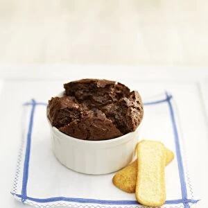 Chocolate souffle served in ramekin with two biscuits on napkin