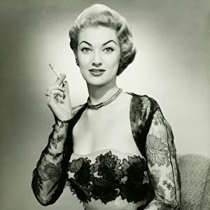 Young woman wearing evening dress smoking cigarette, (B&W), portrait