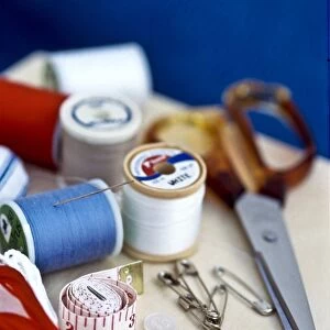 Various bits of sewing kit, including threads, needles and scissors on wooden box