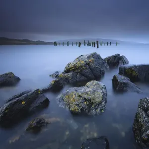 El tiempo tormentoso con nubes de lluvia pesada a la vista con rocas y líquen en primer plano y viejo muelle. El tiempo tormentoso con nubes de lluvia pesada a la vista con rocas y líquen en primer plano y viejo muelle.